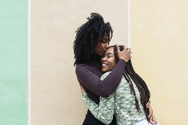 Woman kissing friend standing in front of wall - PNAF03960