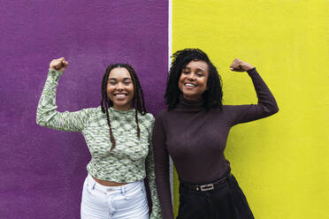 Happy friends flexing muscles in front of purple and yellow wall - PNAF03963