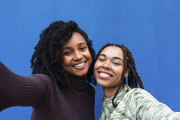 Happy friends taking selfie in front of blue wall - PNAF03983