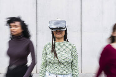 Lächelnde junge Frau in einem Virtual-Reality-Simulator vor einer Wand stehend - PNAF03994