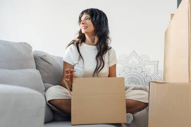 Woman with cardboard box sitting on sofa in living room at home - EGHF00411