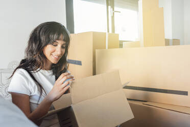 Smiling woman with cardboard box sitting at new home - EGHF00412