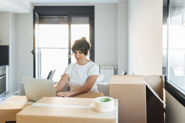 Frau benutzt Laptop auf Karton im neuen Zuhause - EGHF00415