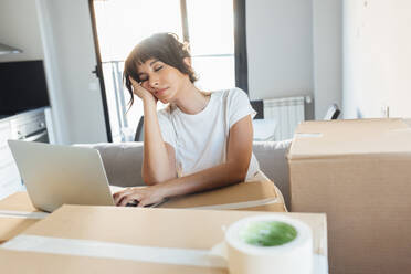 Tired woman with laptop on cardboard at new home - EGHF00417