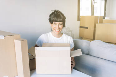 Glückliche Frau mit Kartons im Wohnzimmer sitzend zu Hause - EGHF00425