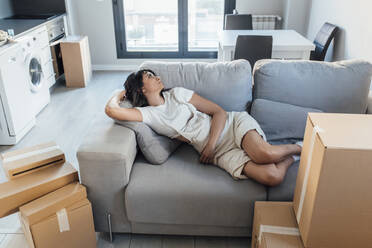 Frau liegt auf dem Sofa im Wohnzimmer ihres neuen Zuhauses - EGHF00441
