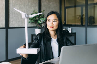 Mature businesswoman examining wind turbine model at office - MEUF06042