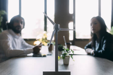 Wind turbine model on desk with colleagues in background at office - MEUF06045