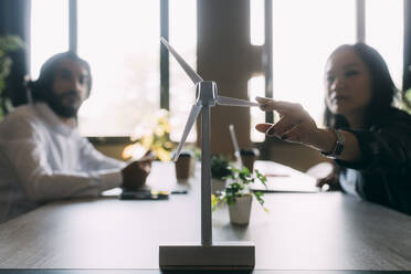 Businesswoman discussing over wind turbine model with colleague at work place - MEUF06046