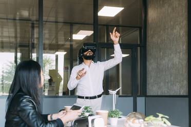 Geschäftsmann gestikuliert mit VR-Brille bei einem Kollegen im Büro - MEUF06081