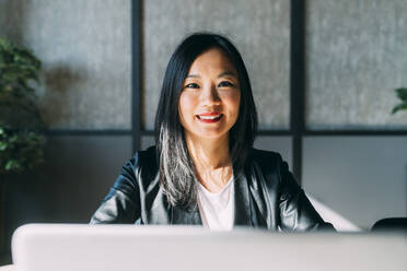 Lächelnde Geschäftsfrau mit Laptop im Büro - MEUF06091