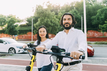 Businessman and businesswoman with electric push scooters on footpath - MEUF06112