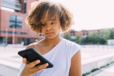 Afro-Frisur mit Smartphone an einem sonnigen Tag - MEUF06124