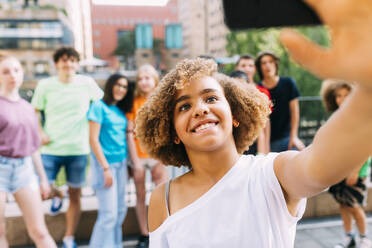 Smiling girl with friends taking selfie through mobile phone - MEUF06178