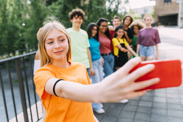 Lächelndes blondes Mädchen nimmt Selfie durch Handy mit Freunden - MEUF06180