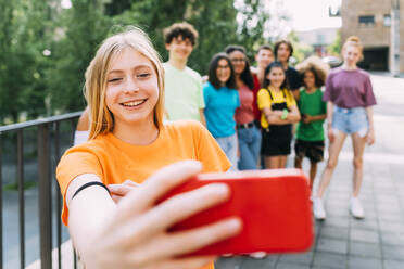 Happy blond girl taking selfie through mobile phone with friends - MEUF06181