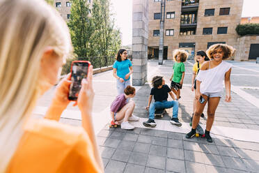 Mädchen mit Smartphone fotografiert Freunde, die auf einem Parkplatz Spaß haben - MEUF06199