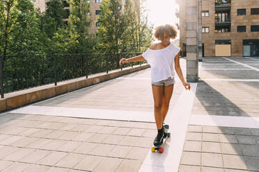 Mädchen mit Afro-Frisur auf dem Skateboard an einem sonnigen Tag - MEUF06205