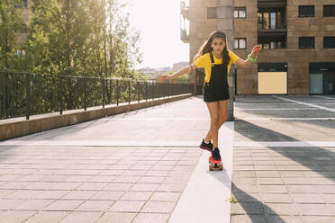 Mädchen auf dem Skateboard vor einem Gebäude an einem sonnigen Tag - MEUF06207