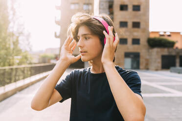 Junge mit drahtlosen Kopfhörern vor einem Gebäude stehend - MEUF06216