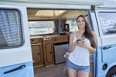 Smiling woman holding mobile phone in motor home doorway - FMOF01471