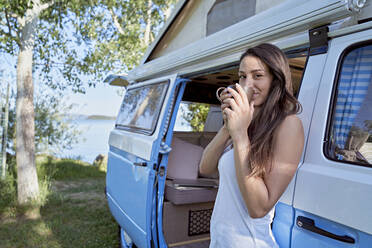 Woman drinking coffee at camper van doorway - FMOF01472