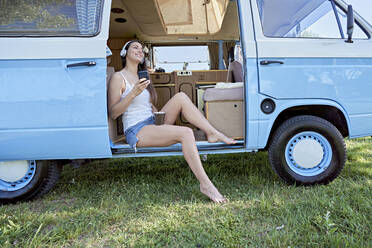 Woman listening music through headphones in camper van - FMOF01473