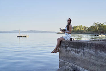 Junge Frau mit Buch auf Steg am See sitzend - FMOF01482