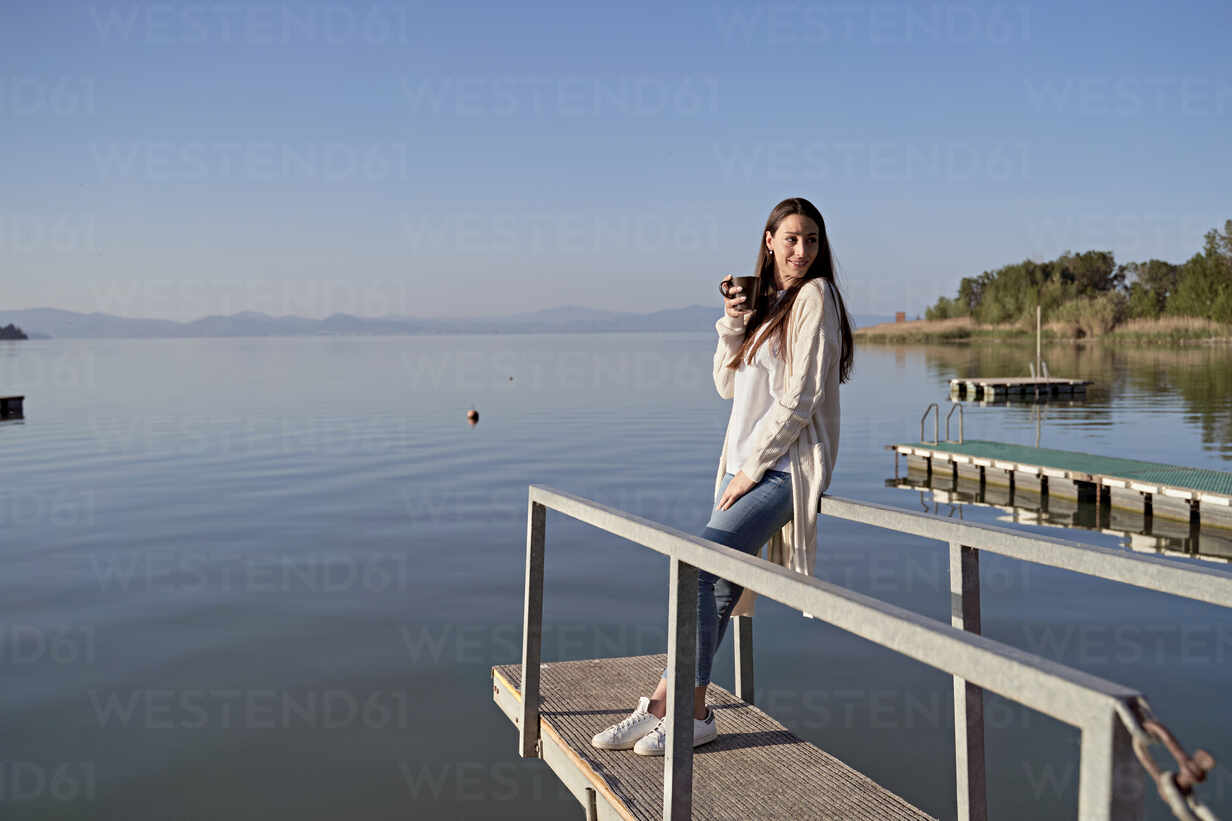 https://us.images.westend61.de/0001681784pw/woman-with-coffee-cup-standing-on-jetty-over-lake-FMOF01492.jpg