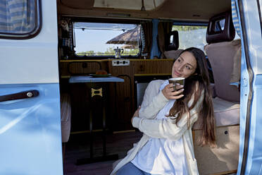 Woman with coffee cup day dreaming at motor home doorway - FMOF01499