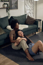 Lesbians sitting together in front of sofa at home - DSHF00479