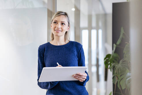 Businesswoman with digital tablet in office thinking - DIGF17931