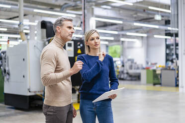 Businessman and businesswoman with digital tablet talking in factory - DIGF17946