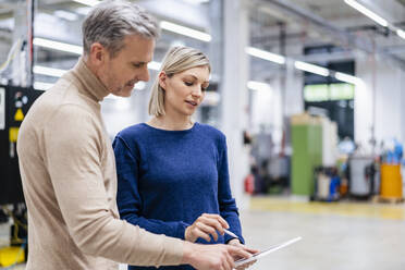 Geschäftsmann und Geschäftsfrau teilen sich ein digitales Tablet in einer Fabrik - DIGF17947