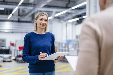 Geschäftsfrau mit digitalem Tablet, die einen Kollegen in einer Fabrik anlächelt - DIGF17957