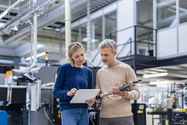 Businessman with device and businesswoman with digital tablet talking in factory - DIGF17961