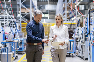 Businessman and businesswoman with digital tablet talking in factory - DIGF17988