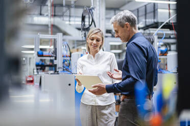 Businessman and businesswoman with digital tablet talking in factory - DIGF17990