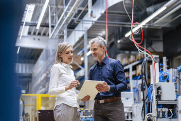 Businessman and businesswoman with digital tablet talking in factory - DIGF17991