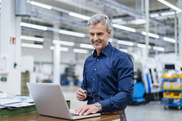 Mature businessman using laptop in factory - DIGF18001