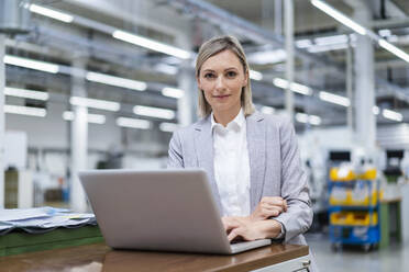 Portrait of businesswoman with laptop in factory - DIGF18012