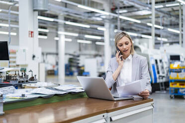 Businesswoman with laptop on the phone in factory - DIGF18014