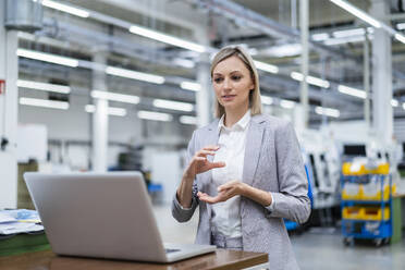 Businesswoman gesturing during video call on laptop in factory - DIGF18017