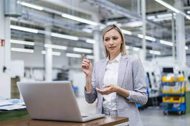 Businesswoman gesturing during video call on laptop in factory - DIGF18018