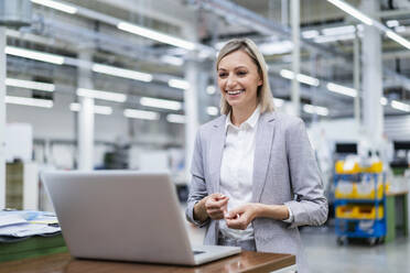 Happy businesswoman looking at laptop in factory - DIGF18019