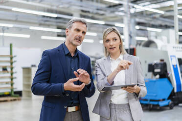 Businesswoman with digital tablet and businessman talking in factory - DIGF18022