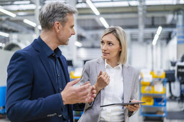 Businesswoman with digital tablet and businessman talking in factory - DIGF18023