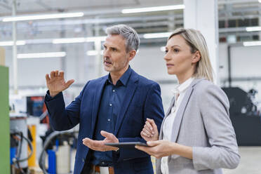 Businesswoman with digital tablet and businessman talking in factory - DIGF18024