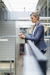 Geschäftsfrau lehnt an einem Geländer in einer Fabrik und benutzt ein digitales Tablet - DIGF18043