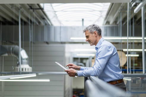 Businessman leaning on railing in factory using digital tablet - DIGF18046